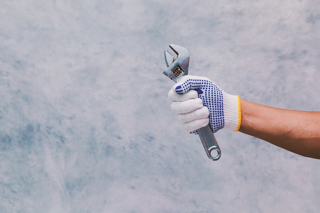 Hand holding a sliding wrench on bare cement wall background