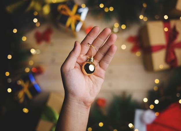 Hand Holding Small Gold Bauble Above Christmas Decoration. Top View