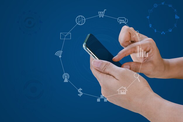 Hand holding smart phone with blurred social media and technology icons on blue color background.