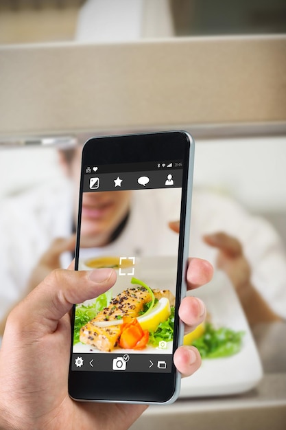 hand holding smartphone against chef handing salmon dinner through order station