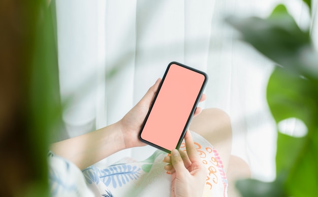 Hand holding smartphone mockup of blank screen on table.