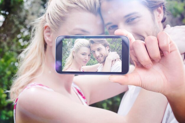 Foto smartphone della tenuta della mano che mostra contro la coppia sveglia che sta fuori che abbraccia sorridente alla macchina fotografica