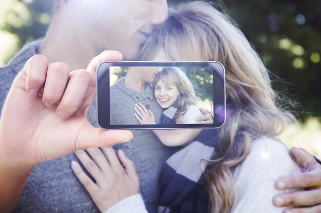 Mano che tiene lo smartphone che mostra contro la donna carina che sorride alla macchina fotografica con il suo fidanzato