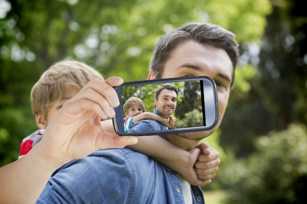 Hand holding smartphone showing father carrying young boy on back at park