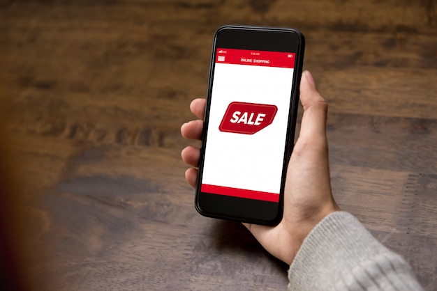 Hand holding smartphone showing sale promotion label on screen 