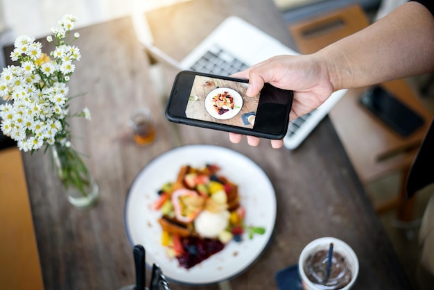 Photo hand holding smartphone taking french toast topping mixed fruit ice cream italian soda on wooden table in modern bright kitchen interior