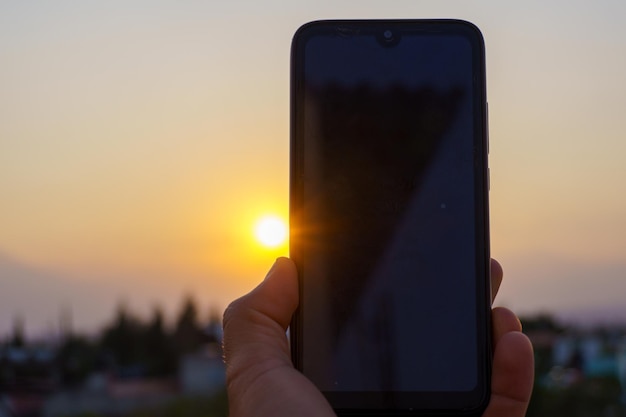 Hand holding a smartphone taking a photograph at sunset
