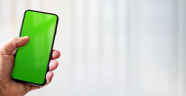 빈 녹색 화면이 있는 스마트폰을 들고 있는 손 사무실 배경 가로 배너