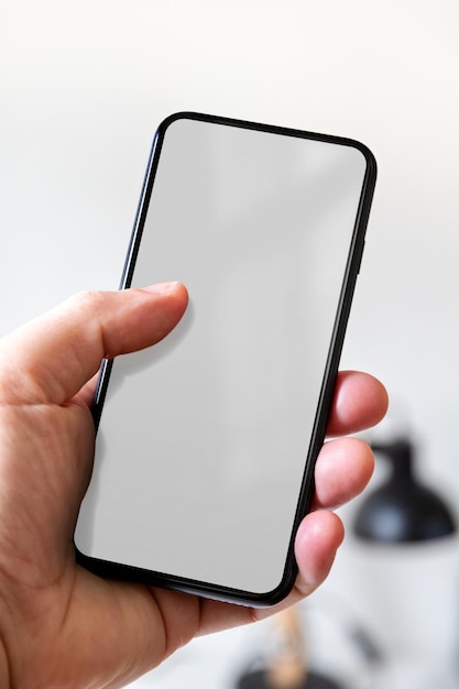 Hand holding a smartphone with blank grey screen Office background