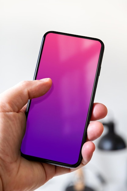 Hand holding a smartphone with blank pink and purple screen Office background