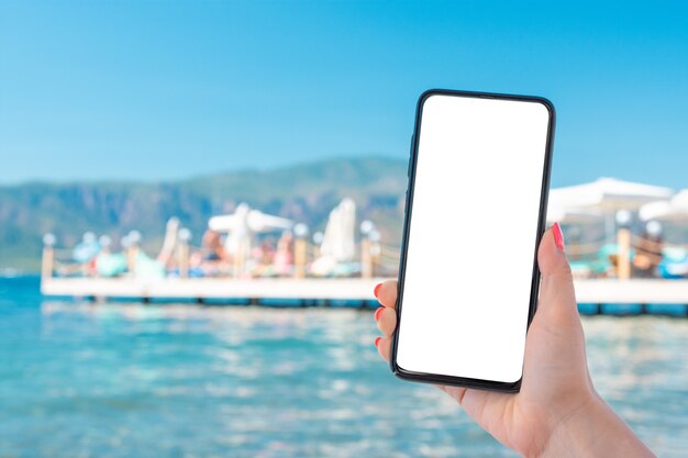 hand holding smartphone with blank screen over the sea and blue sky.