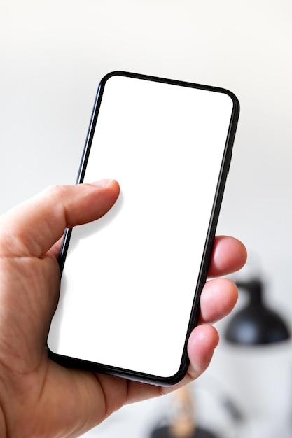 Hand holding a smartphone with blank white screen Office background