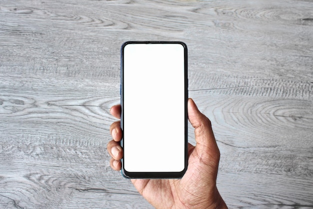 Hand holding smartphone with blank white screen on wooden table background