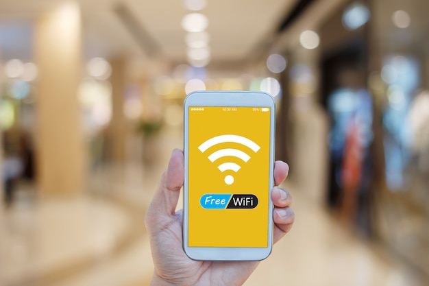 Hand holding smartphone with Free WiFi on screen over blurred in shopping mall background