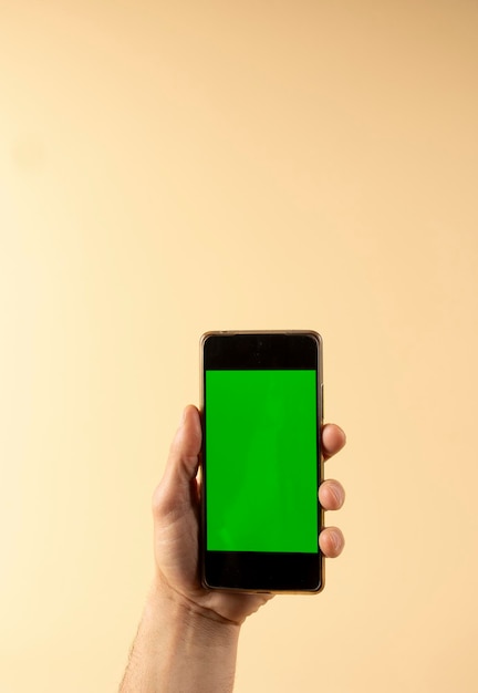 写真 コピースペースのパステル色の背景に隔離された緑色の画面のスマートフォンを手で保持するxa