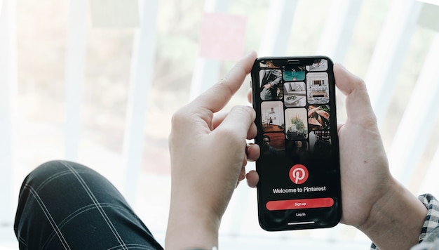 Hand holding smartphone with Pinterest app on the screen. Pinterest is an online pinboard that allows people to pin their interesting things