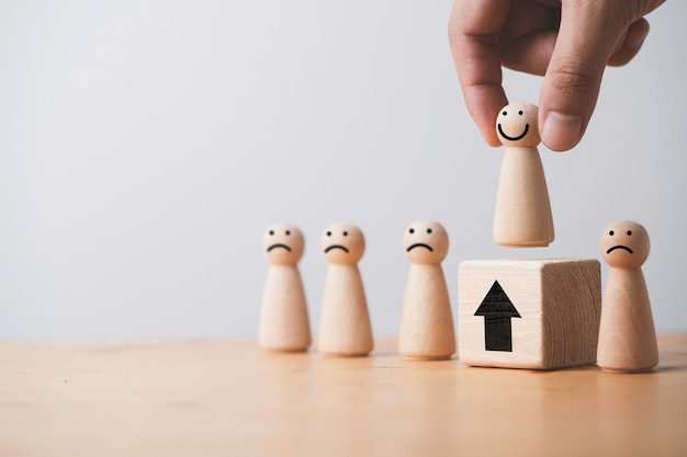 Hand holding smile wooden figure to above of wooden cube which higher position for promotion from staff to management and human development concept