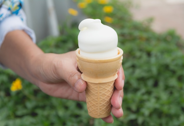 Hand holding soft white milk cream ice cream cone in summer day on nature background.