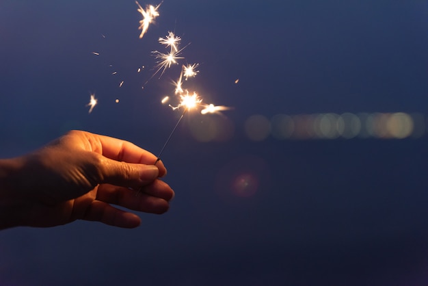 Hand holding a sparkler on beach during sunset. Celebration concept.