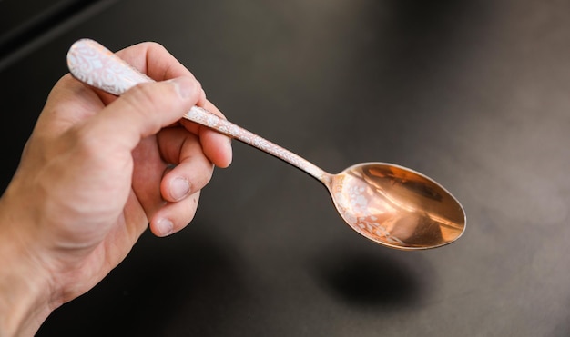 A hand holding a spoon with a copper handle.