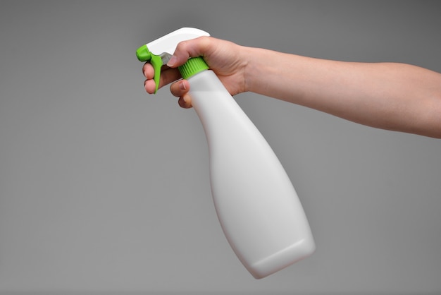 Foto mano che tiene la bottiglia di plastica spray isolata su sfondo grigio mano femminile con spruzzatore isolato