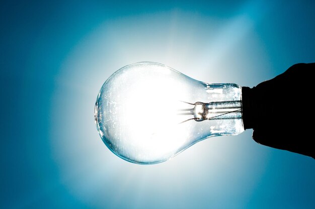 Hand Holding Standard Incandescent Light Bulb on Blue Background