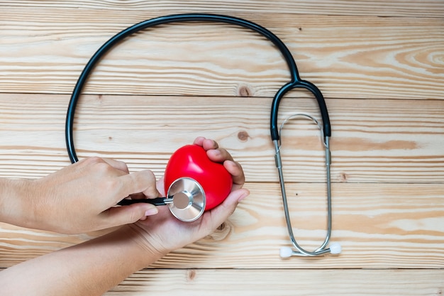 Hand holding Stethoscope with Red heart shape on wooden background. 