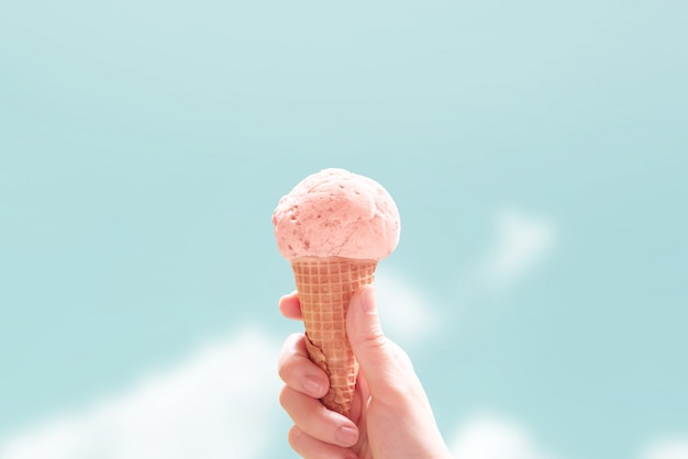 Foto passi il cono gelato della fragola della tenuta su cielo blu di estate. stile minimal, copia spazio.