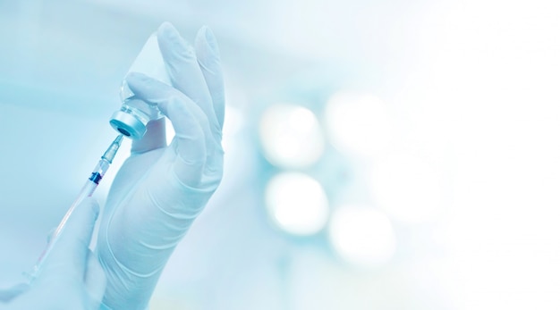 Photo hand holding syringe and medicine vial prepare for injection in operating room with surgery lamp background