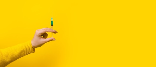 Hand holding syringe with medicine over yellow background, 