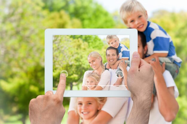 Foto mano che tiene il tablet pc che mostra la famiglia felice nel parco