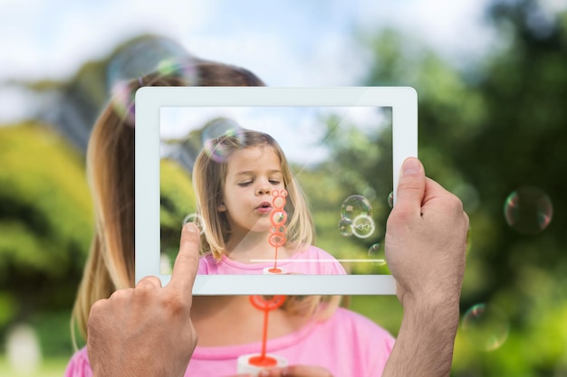 Hand holding tablet pc showing little girl playing with bubbles in the park