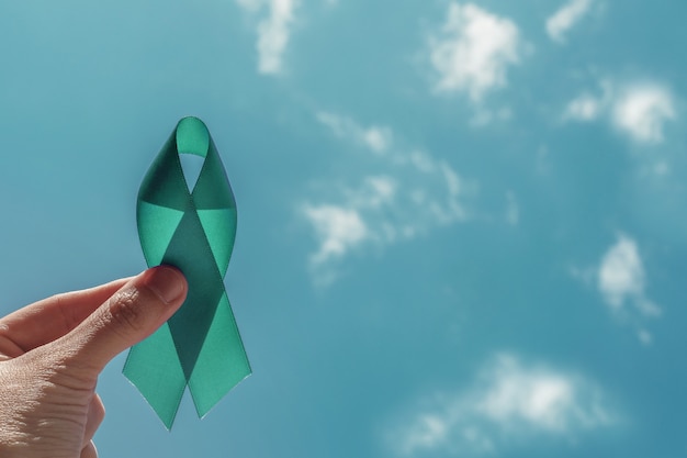 Рука Teal Ribbon над голубым небом