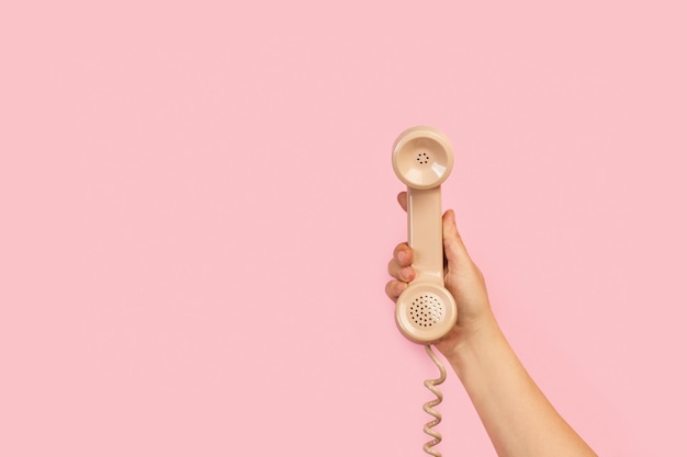 A hand holding a telephone against a pink background