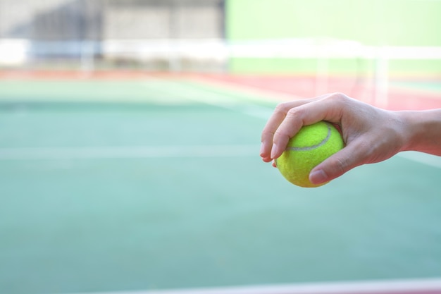 Hand holding tennis ball on court background 