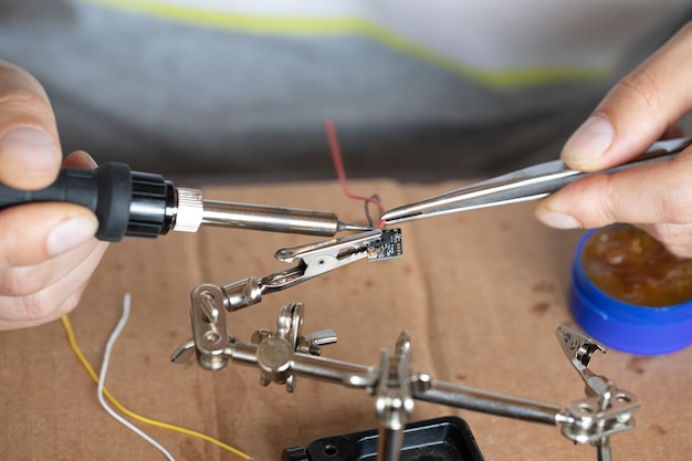 The hand holding the tin a soldering iron solder the chip in place a man solders a wire to a microcircuit