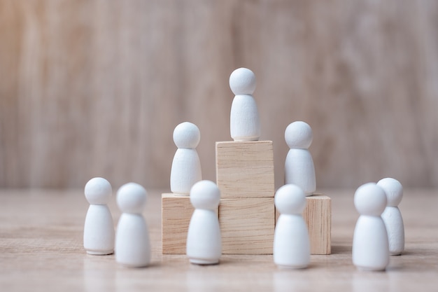 Hand holding top of businessman leader with crowd of wooden men.