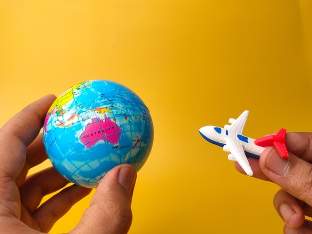 Hand holding toys plane and world globe on a yellow\
backgroundholidays and travel concept