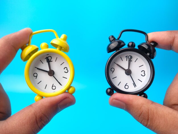 Hand holding two alarm clock on blue background