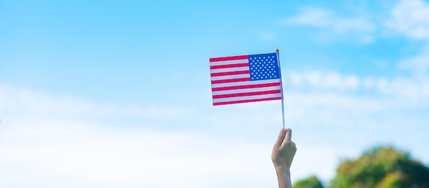 Hand holding united states of america flag on blue sky\
background usa holiday of veterans memorial independence fourth of\
july and labor day concept