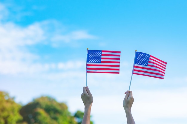 Hand holding united states of america flag on blue sky\
background usa holiday of veterans memorial independence fourth of\
july and labor day concept