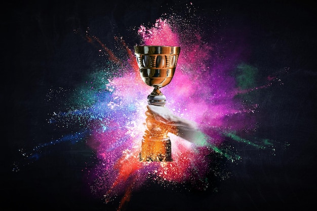 Photo hand holding up a gold trophy cup against dark background. mixed media