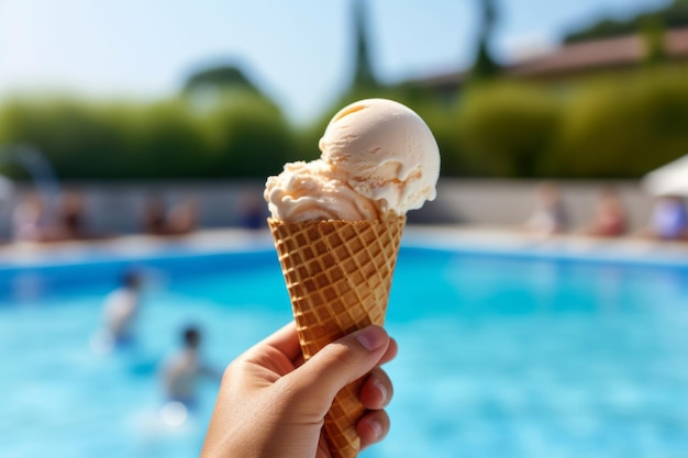 A hand holding a vanilla ice cream cone in front of a pool