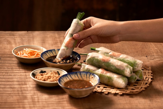 Hand holding Vietnamese spring roll above the bowl with dipping soy sauce