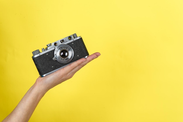 a hand holding a vintage photo camera on a yellow background with a space for a text