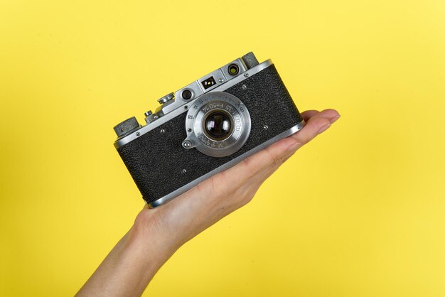 a hand holding a vintage photo camera on a yellow background with a space for a text