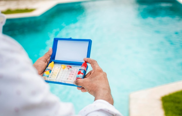 Mano che tiene il kit per il test dell'acqua su uno sfondo sfocato della piscina mano che tiene un tester per il ph e il cloro della piscina persona che tiene un kit completo per il test dell'acqua con lo sfondo della piscina sfocato