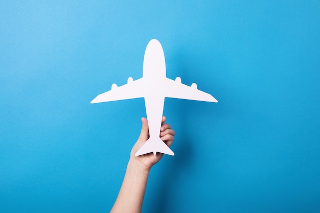 Hand holding white airplane over blue background, travel concept