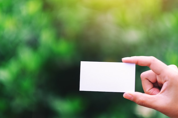 A hand holding a white blank business card with green nature background
