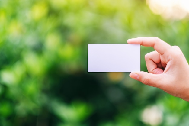 A hand holding a white blank business card with green nature background